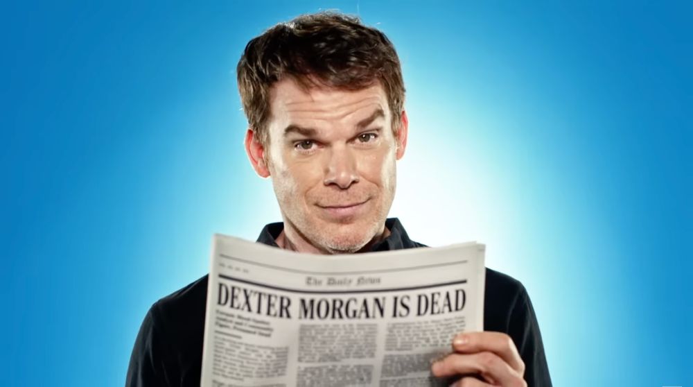 Michael C Hall as Dexter Morgan, holding a newspaper with the headline "Dexter Morgan is Dead" while raising his eyebrows and smirking
