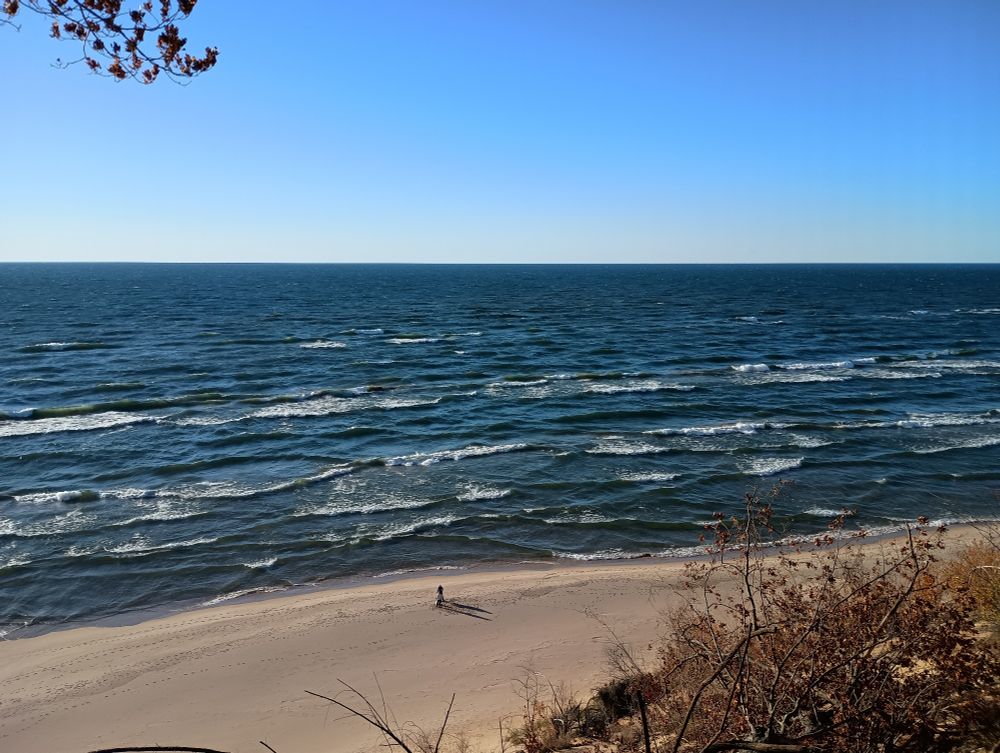 Lake Michigan from the top of a sand dune. Two people stand on the beach below. There are crashing waves all over.