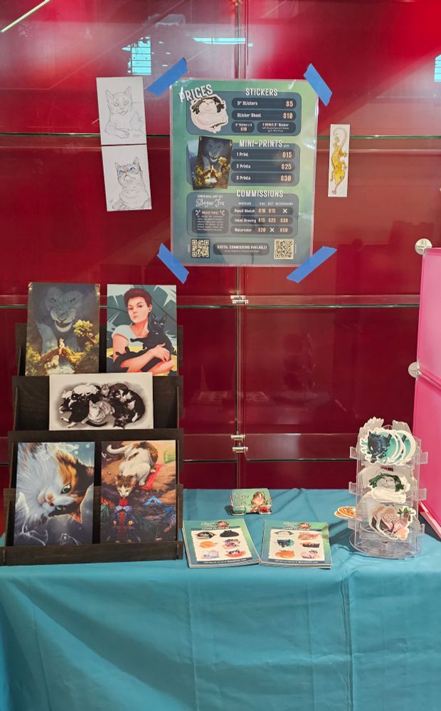 A booth holding stickers and prints in front of a glass case. 