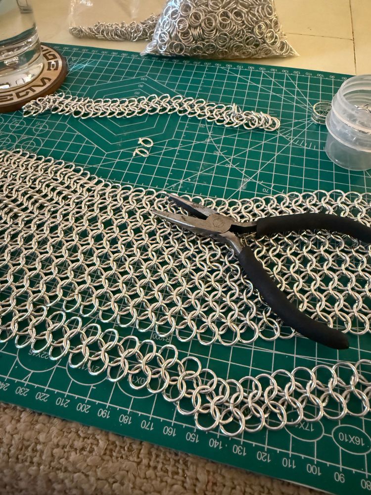 My current chain mail project, which will be a hip kit for my wife. The piece of mail sits on top of a craft cutting mat, with my jewelry pliers nearby.