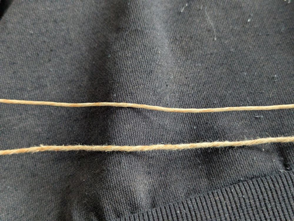 Deux parties du fil de coton en question : celle du bas est d'apparence lâche et un peu "fluffy". Celle du haut, enduite de cire, est lisse, plus dense et plus raide.