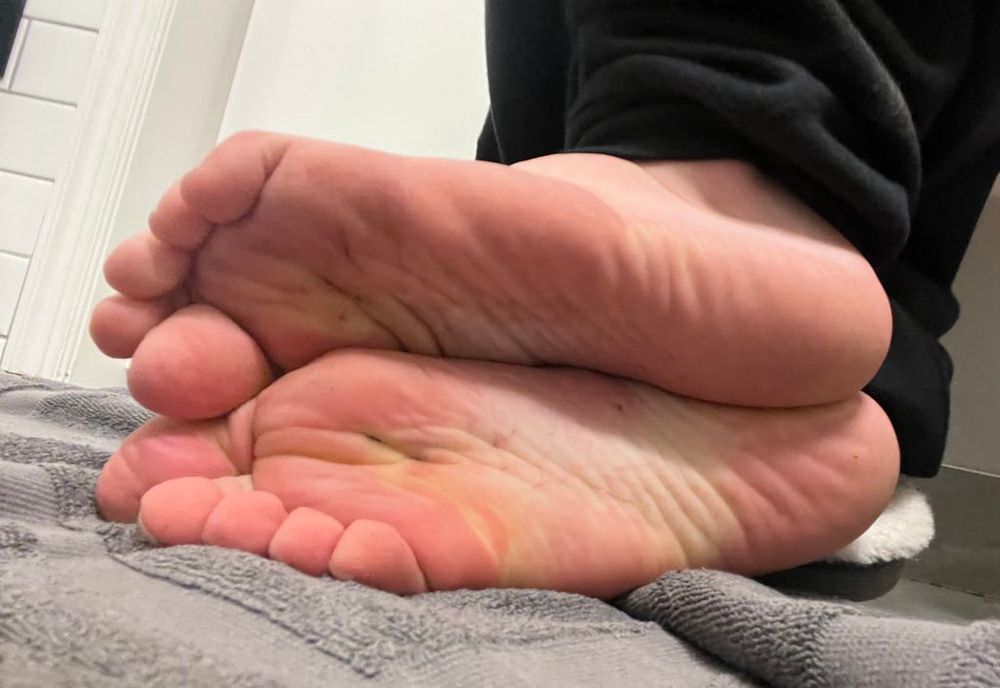 Soles facing camera, feet resting on gray towel, shower wall visible in background 