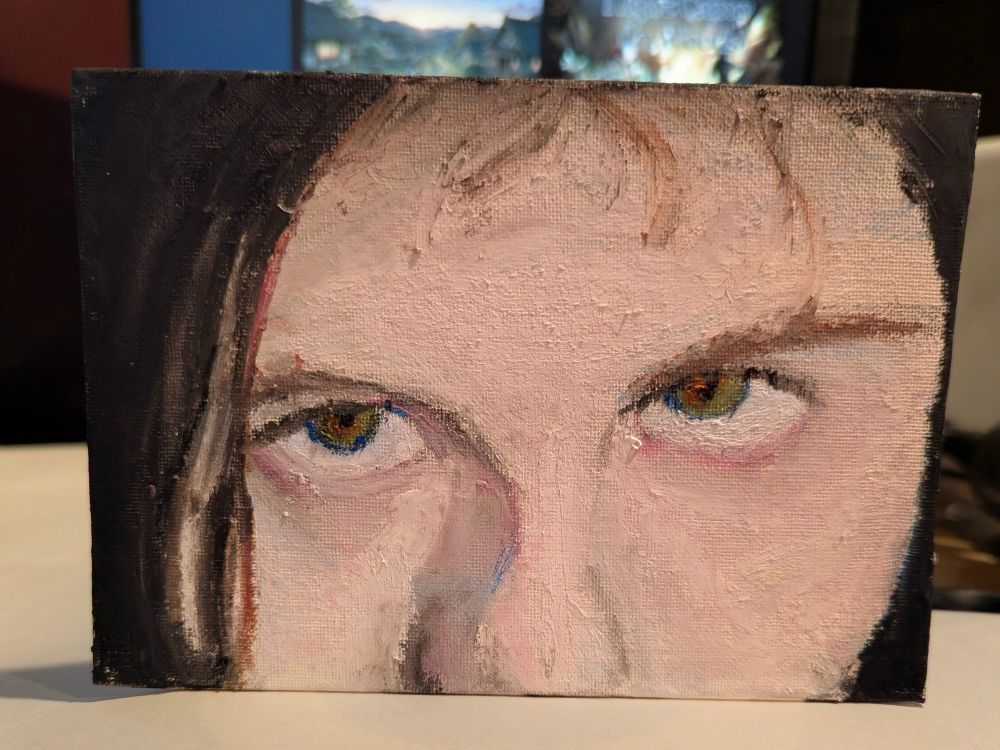 A small erect canvas with a self-portrait of the artist featuring part of their face from their forehead to just before the bottom of their nose. The image has the reference looking upwards and to the side at an intense angle.