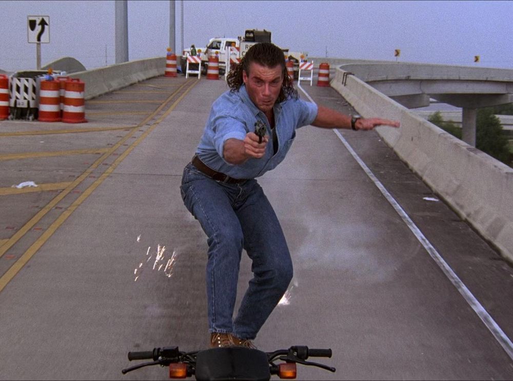 van damme in hard target standing on a motorcycle aiming a gun