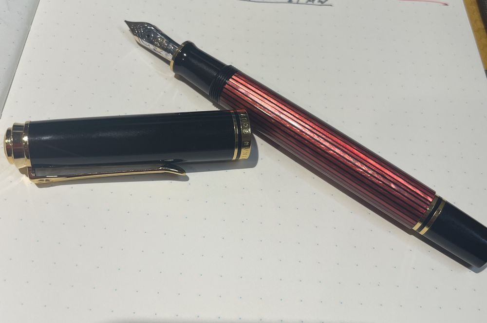 top down photo of a red and black fountain pen with black and gold cap on a dot grid notebook