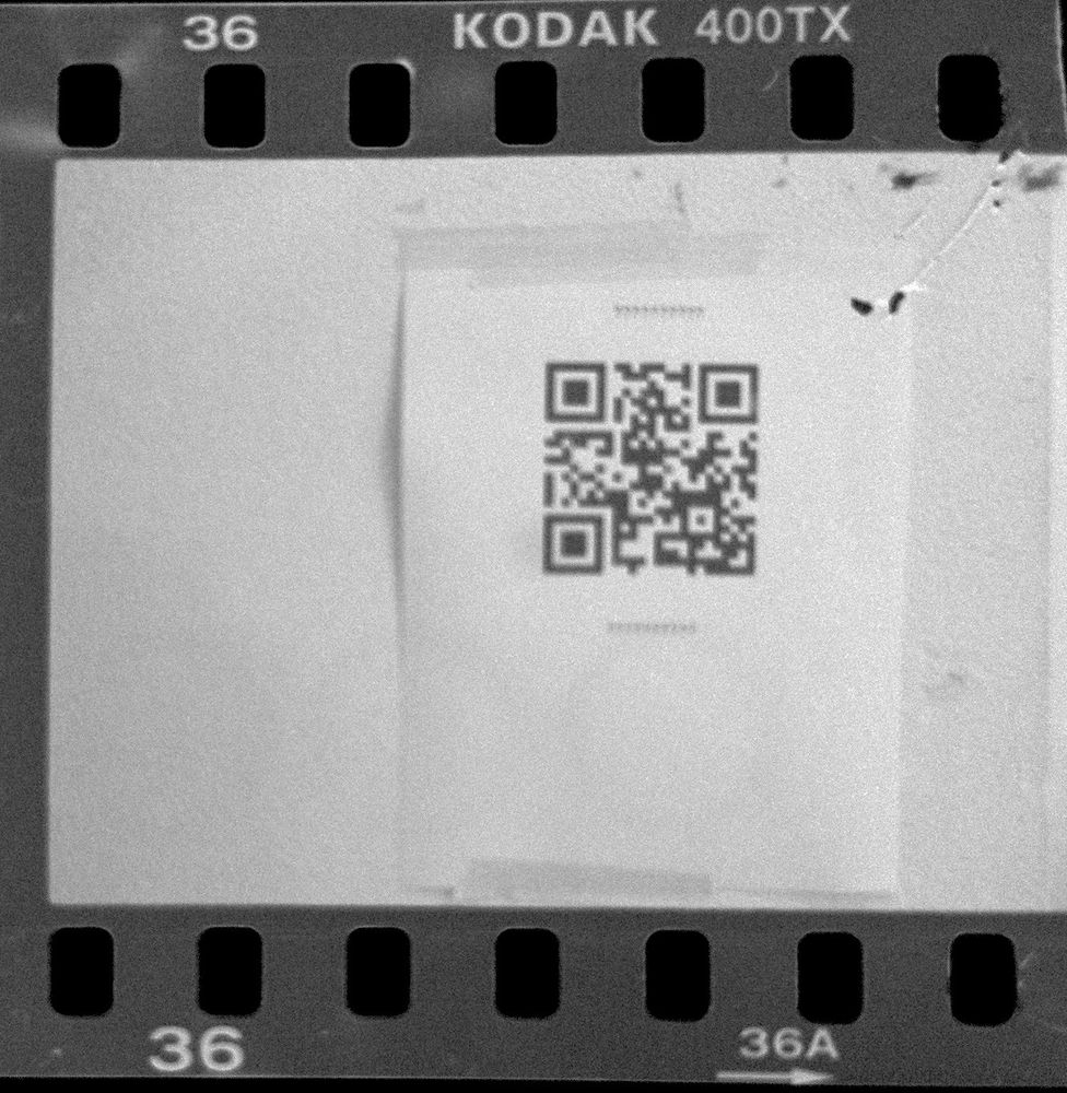 a reversed image of a photographic negative showing a piece of paper taped to the wall containing a QR code