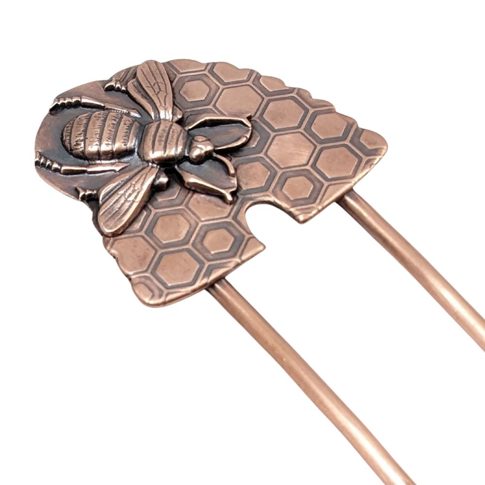 Copper hair fork. The design at the top is a copper beehive dome shape with an impressed honeycomb pattern. On top of the dome there is a very large copper honeybee.