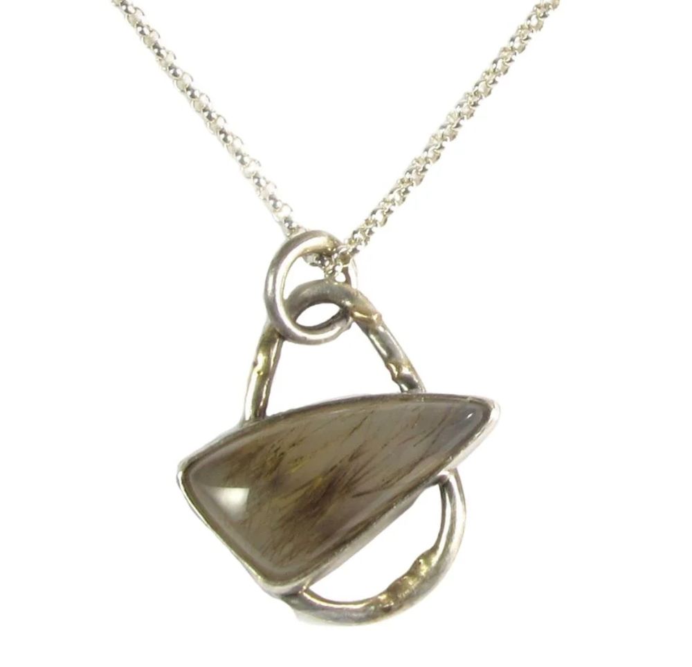 Sterling silver pendant. The focus of the pendant is a stone in a modified triangle shape - the two short sides are straight and the long side is gently curved to form an arch. The stone is set on a teardrop shaped round wire and at an angle so the arch is at the top. The wire has little globs of fourteen karat gold melted onto it. The stone is a milky white and inside it are fine, straight dendrites that look like brown hair.

