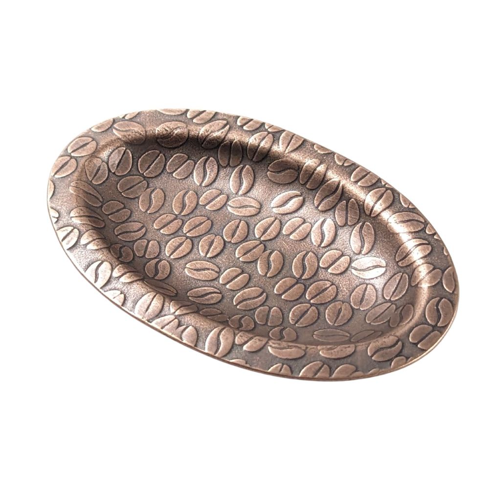 Copper ring dish. It is oval shaped with a flat lip around the edge, and is covered in an impressed design of coffee beans.
