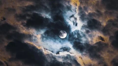 Photo of a full moon behind clouds that appear to be mixed with smoke from a fire. 