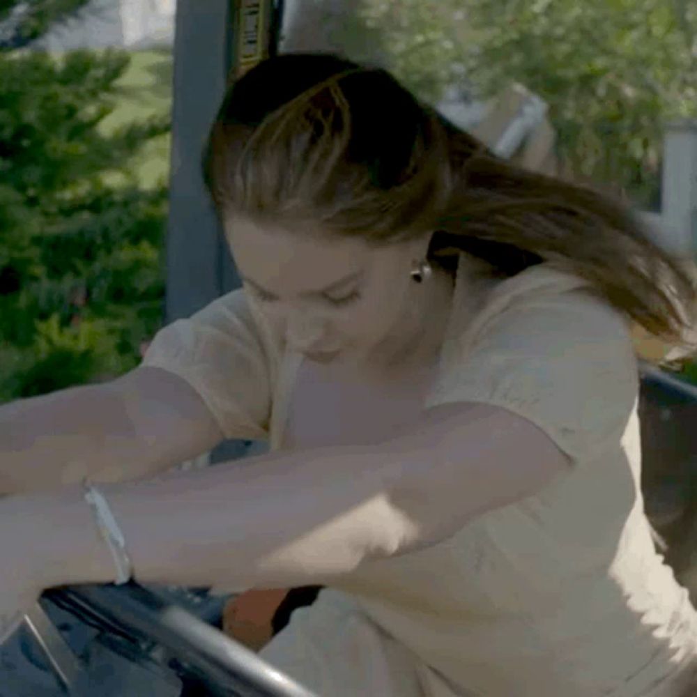 a woman in a white shirt is sitting in a vehicle with her arms outstretched