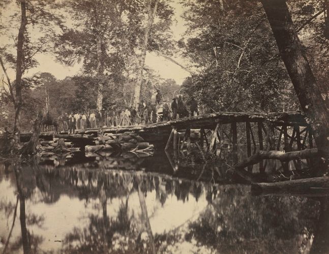 In this complex composition, David B. Woodbury merged the documentation of an event with his desire to record an impressive landscape. The image depicts a precarious, yet essential military log bridge that traverses a swamp created by the accumulated waters of the Chickahominy River, located southeast of Richmond, Virginia. Constructed under difficult physical conditions, the structure was later destroyed by floodwaters caused by heavy rains. The workers involved with the structure's construction are positioned in a single line so that each person is identifiable; however, reduced to diminutive size by the camera's distant viewpoint, the workers appear to be dominated by their natural environment. This image appeared in the first volume of a two-volume set of 100 Civil War photographs published between 1865–66 by Alexander Gardner (1821–1882), who printed the negatives and compiled the album, which included work by a number of other photographers.