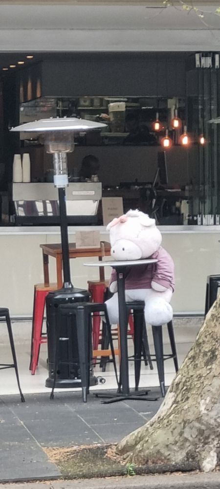 A very large soft toy unicorn appearing to be asleep at a cafe table 