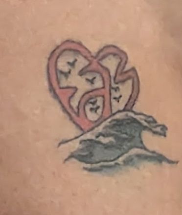 Un tatouage rouge en forme de cœur surfe sur une 🌊.
Il est constitué des lettres FAM et librement inspiré du logo de l' association Fight Aids Monaco créée par la princesse Stéphanie de Monaco.
