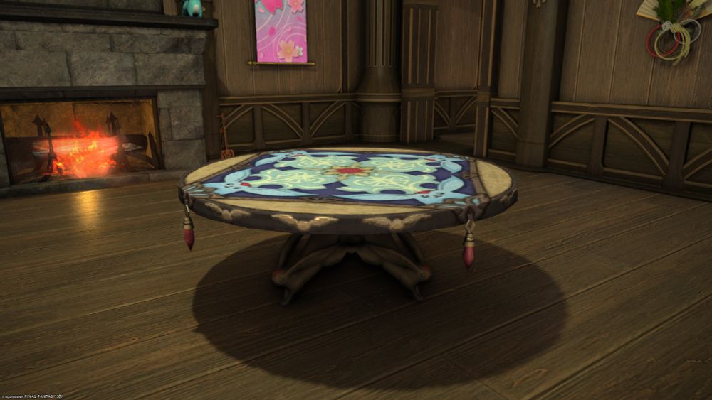 A screenshot from the game Final Fantasy 14 of the Carbuncle Table that I built in the game yesterday. A Carbuncle is a fox-like creature in the Final Fantasy universe. This round wooden table features a square table cloth that has the image of a blue Carbuncle on it in four quadrants. The square table cloth has a dangling ruby pendant at each corner. The table is supported by a cross-shaped cluster of wood that is carved into the likeness of the Carbuncle at the ends of the feet of the table.