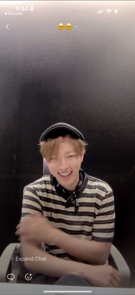 A smiling, seated Hongjoong on pop live, dressed in black and white horizontal stripes, a newsie cap, and a black kerchief tied around his neck. 