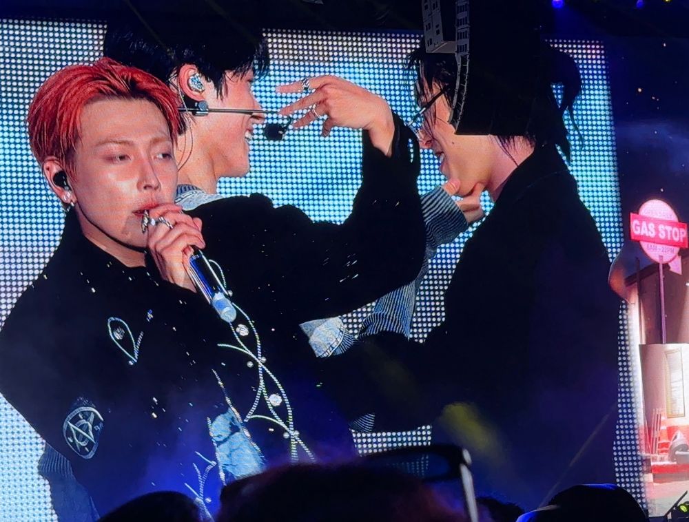 Still of the big screen at Wrigley field during the Ateez concert in July 2025, during “Lemon Drop.” Hongjoong is in the foreground, while Yunho and Mingi are in their own world behind him, facing each other and smiling freely. Yunho has his fingers cupping Mingi’s chin. 