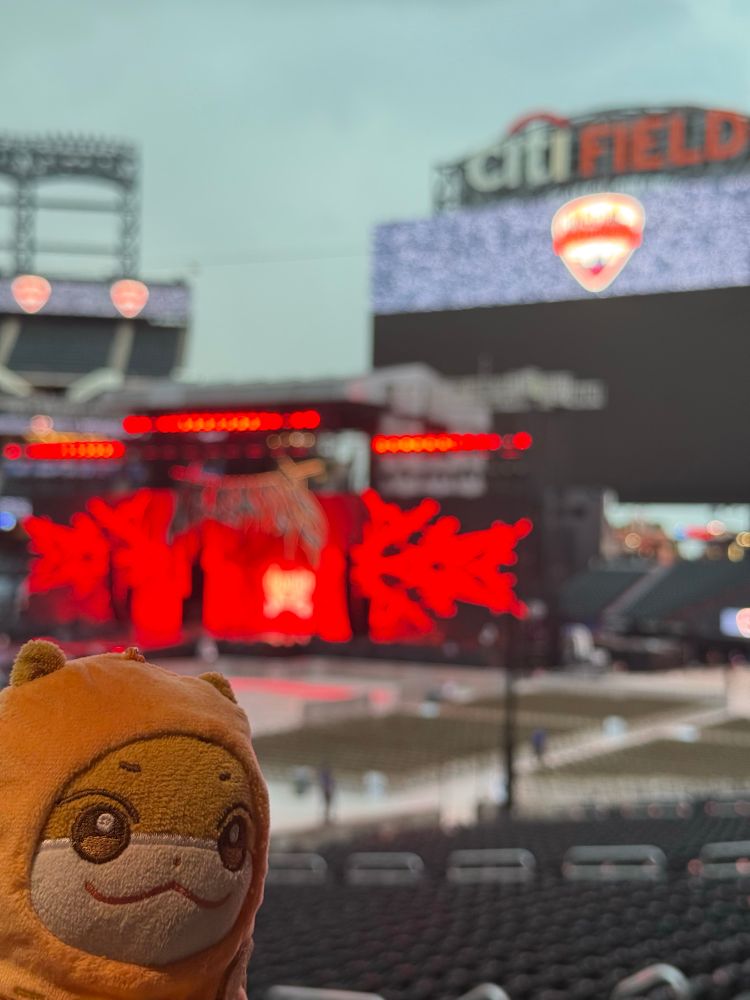 Jjoongrami looking like a menace in the corner of the shot, with the lower bowl and empty Stray Kids stage beyond that, out of focus. Skies are cloudy above that. 