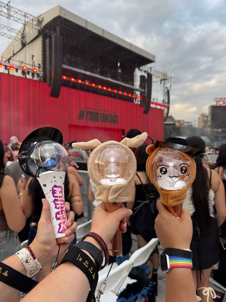 Three defeated lightinies, in matz, Tyudeongi, and Jjoongrami + tiny cowboy hat, posed in front the In Your Fantasy stage. It’s still daylight, before Ateez has come on stage. 