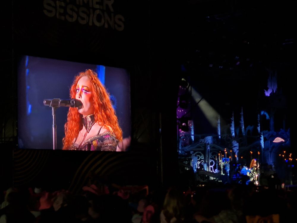A wide view of a white woman on a big screen and on stage