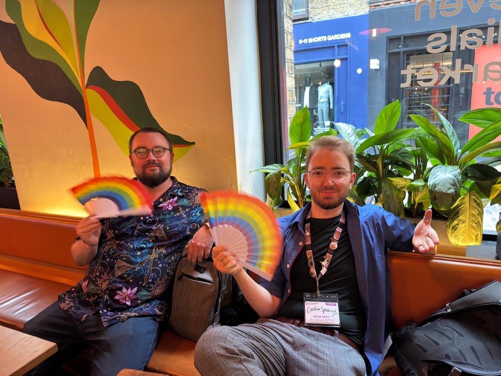Two men sitting on benches waving rainbow fans
