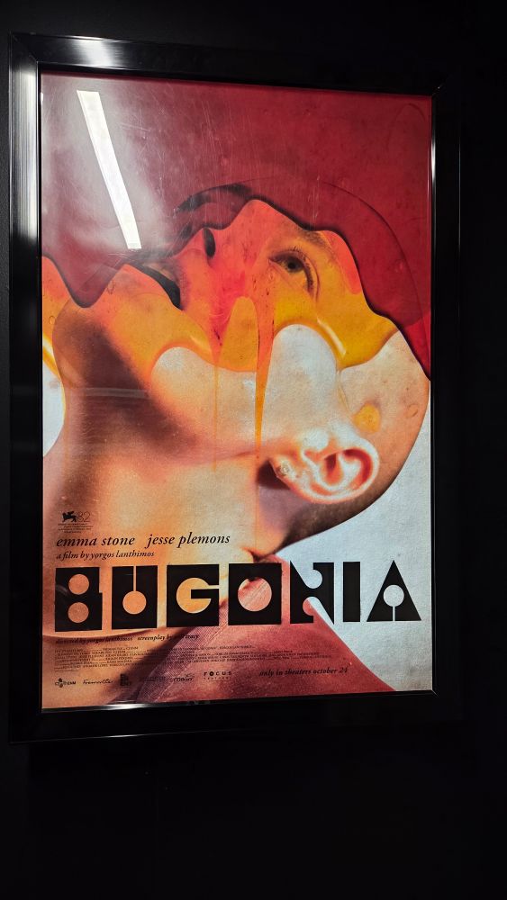 A poster for the movie "Bugonia" featuring Emma Stone with a shaved head with honey pouring over her face. 