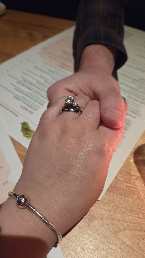 Me and my husband's clasped hands over a menu.  I have on my wedding and engagement rings and a silver bracelet. 