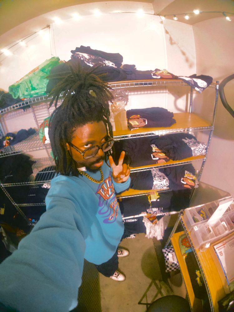 JER taking a selfie in front of a shelf of JER MERCH. 