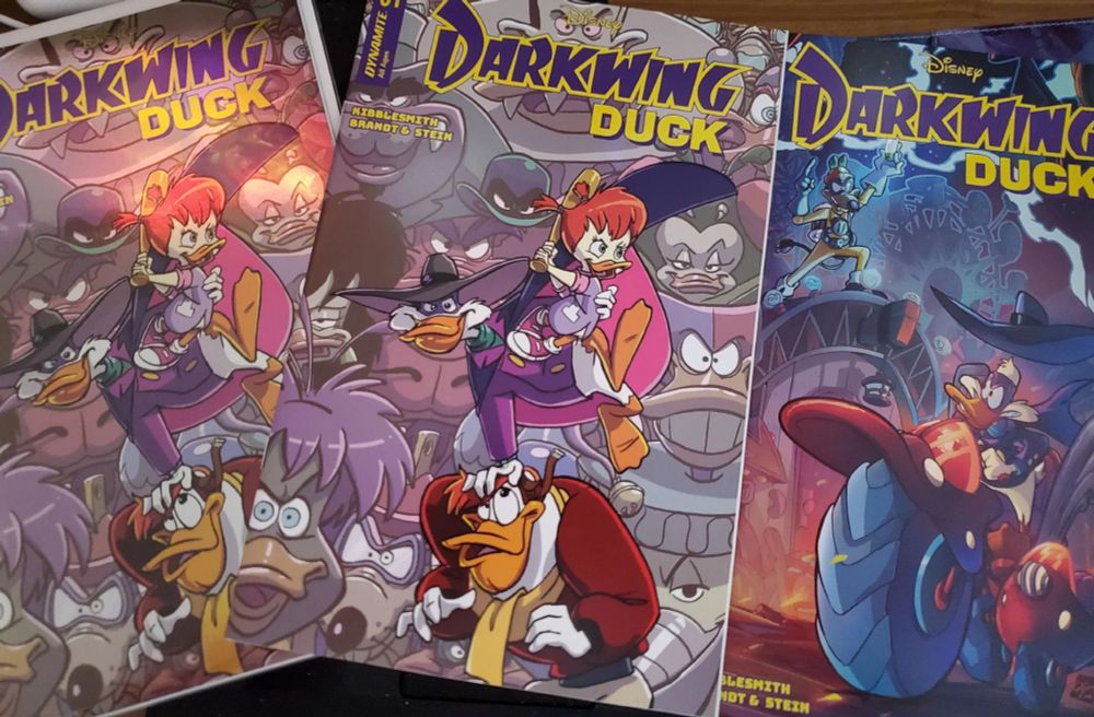 A photo of three versions of the new Dynamite Darkwing Duck comic. From left to right: Foil version of Tad Stones cover, regular version of Tad Stones cover, and a cover by Ciro Cangiolosi. 