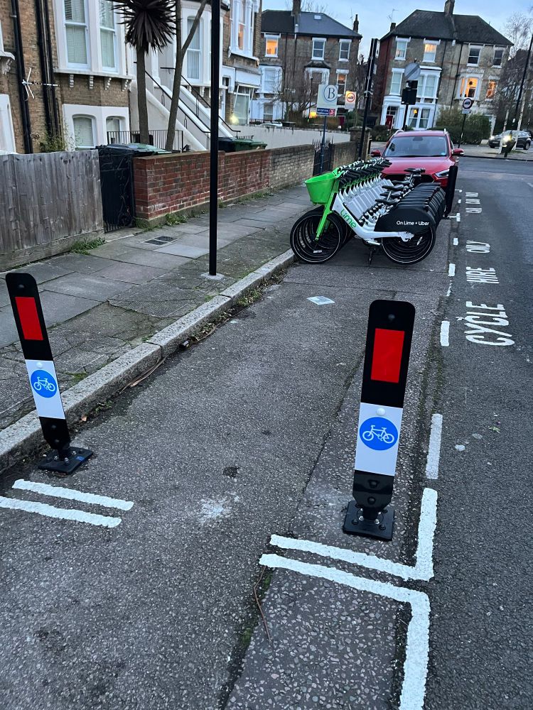 Row of neatly lined up Lime hire bikes in new dedicated off footpath, roadside parking bay next to Car Club bay. 