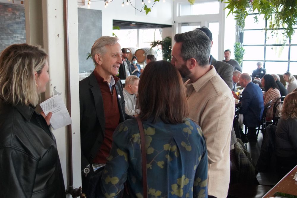 Mayor Keith Wilson engaging with CEIC members in an industrial event space, decorated with string lights and hanging plants.