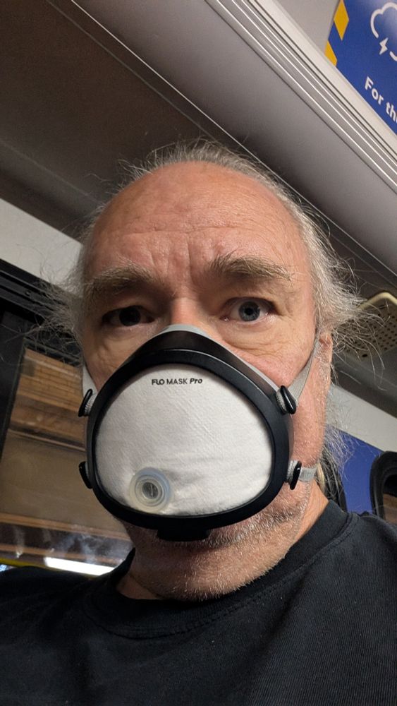 Weird looking old balding man, wearing a black T-shirt and a respirator with a black cover. 