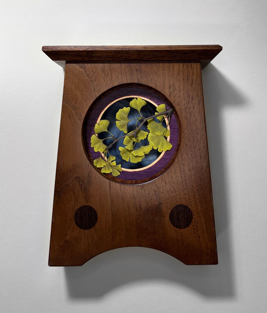 Cut paper ginkgo leaves framed in a wooden clock case, with purple and gold circular mats, and blue background. 