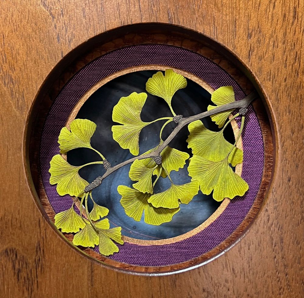 Cut paper green/yellow ginkgo leaves framed in wood, with purple and gold circular mats, and blue swirly background. 