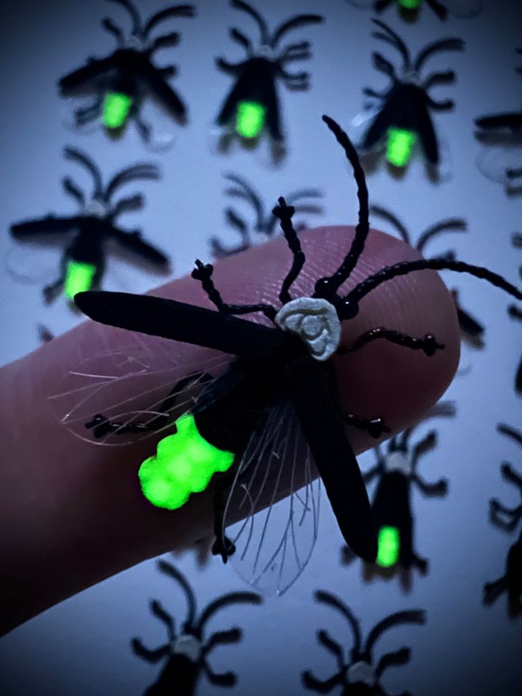 Laser cut firefly insect with glow in the dark paint in low lighting, balancing on a fingertip. 