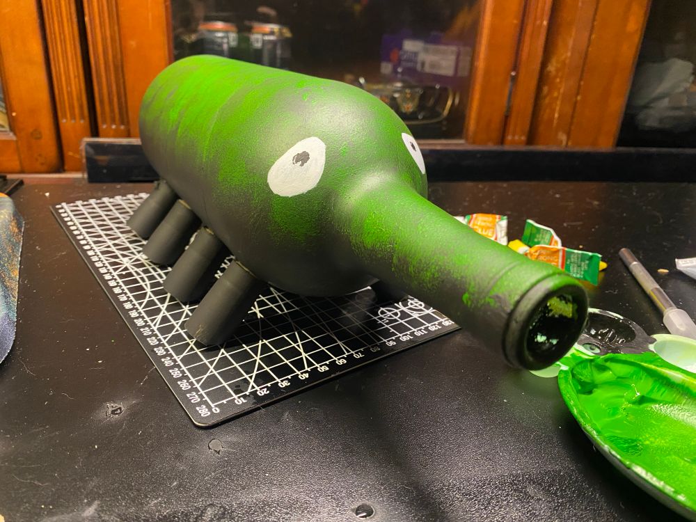 A monster made out of a wine bottle laid on its side and now has 8 feet made of corks! He was painted black and has a mossy top like appearance. Crooked eyes & crooked pupils 