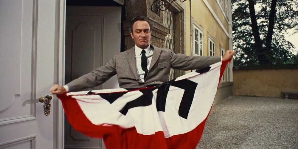 With a grim look of determination, Captain Von Trapp stands before the open door of his chateau, and rips a nazi flag in half.