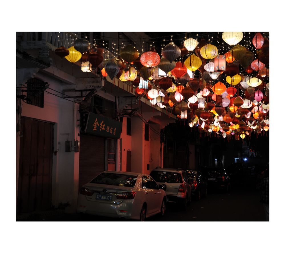 Hundreds of colourful lanterns hanging above the street with cars in the night