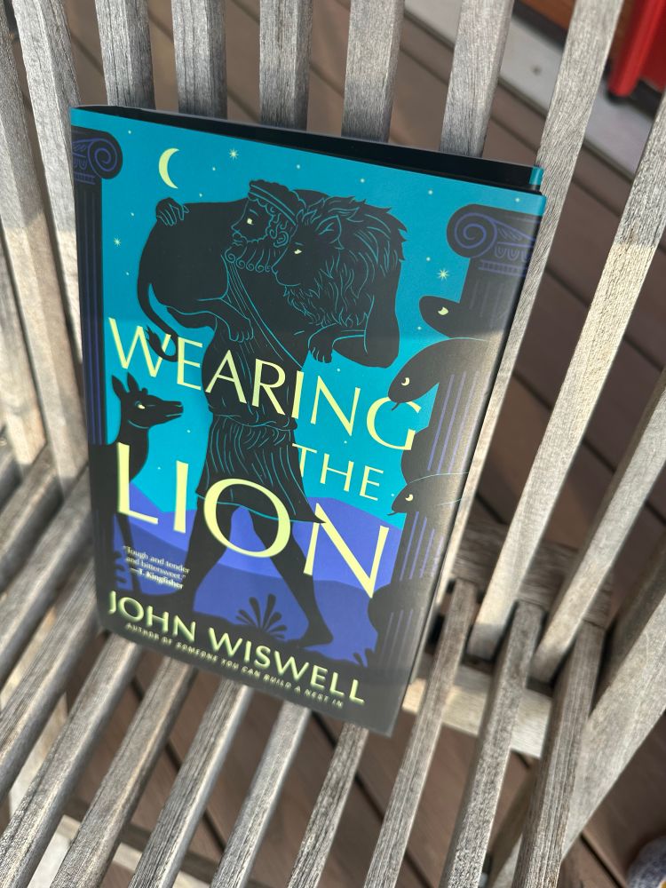 Hardback copy. Wearing the Lion by John Wiswell. Cover has dark etching of man in toga with lion on his shoulders against blue night sky and purple mountains in distance.