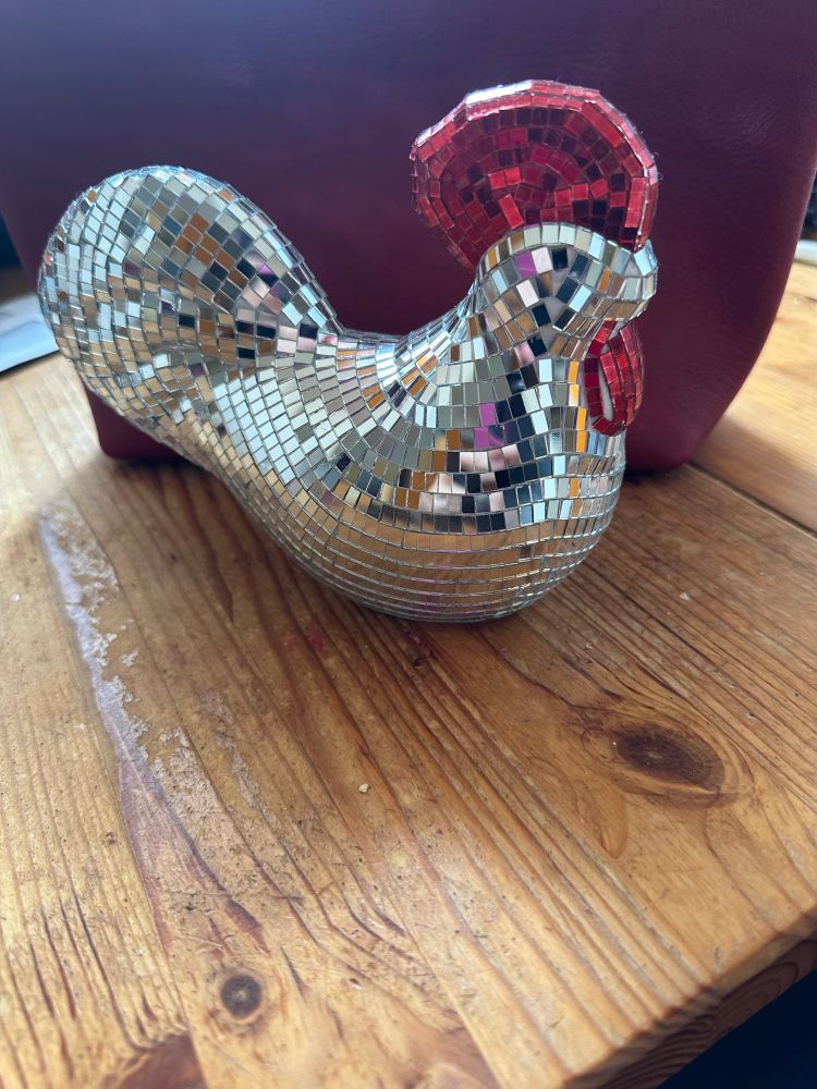Chicken figurine covered with mirror mosaic —similar to disco ball —with red comb and beak.