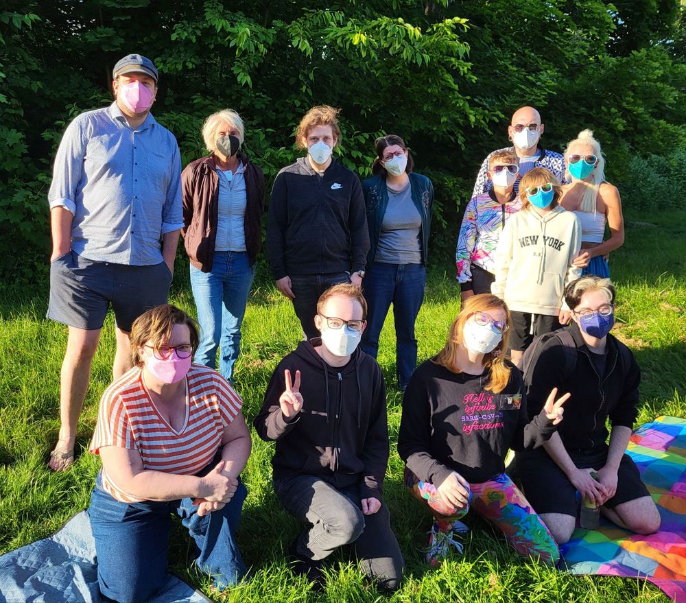 Foto von 12 Personen mit FFP2 Masken auf einer Wiese mit Bäumen im Hintergrund
