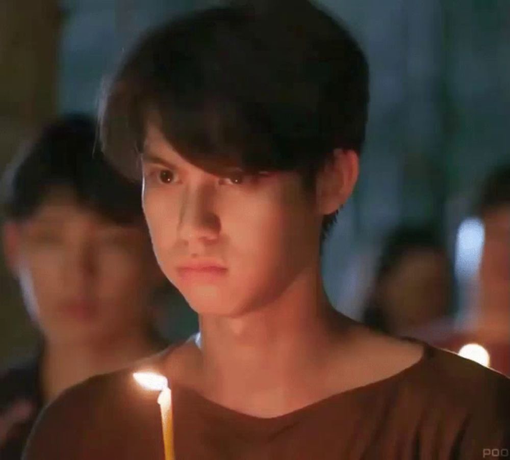 a young man is holding a candle in his hand and looking at it .