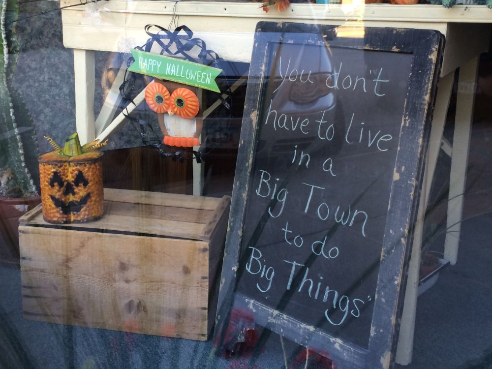 Sandwich board sign in a storefront window, saying "You don't have to live in a Big Town to do Big Things."