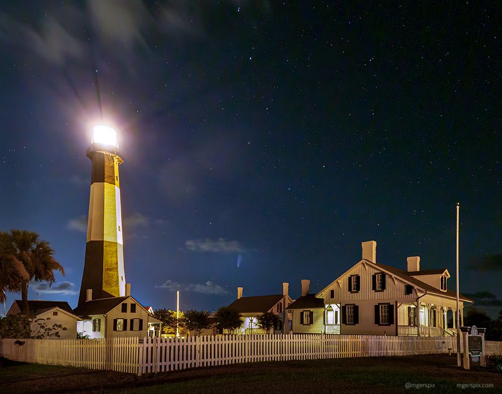 The light station on Tybee Island near Savannah, GA, lit at night with comet Neowise low in the sky near the middle of the frame.
