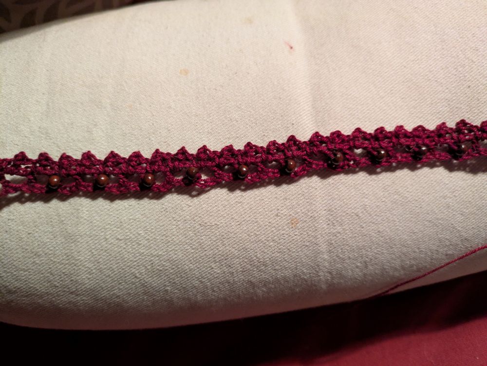 A stretch of wine red crocheted lace, a couple centimeters wide, with small wooden beads interspersed 