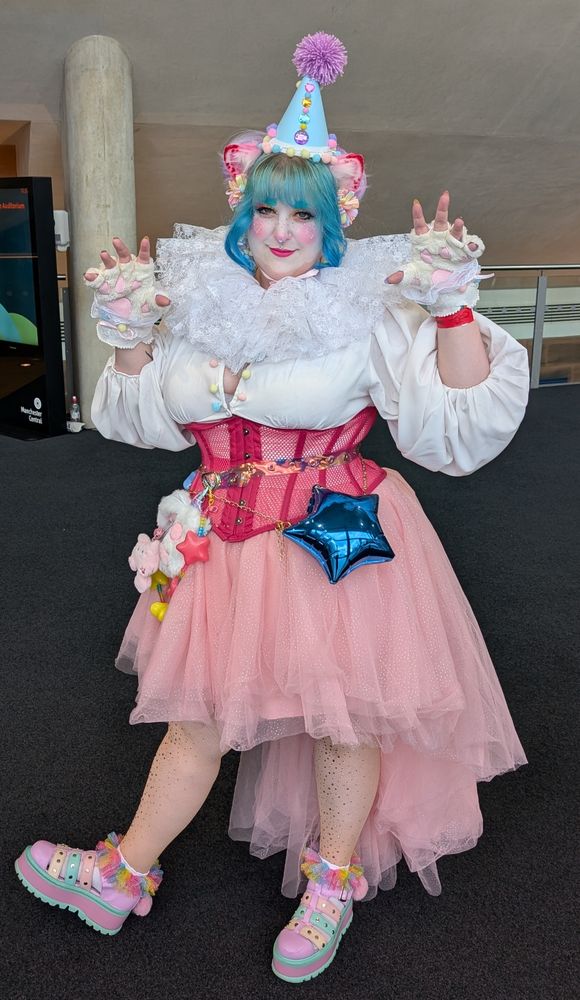 Front view of myself in a blue, purple, pink and yellow party/clown hat, white blouse, pink cat ears, pink corset and skirt and a long white cat tail. 