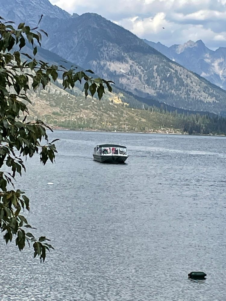 A boat on the waters of Jenny Lake, with mountains rising on the far shore. The boats act as hiker shuttles all day, but three times a day take people on scenic cruises of the lake. The trail to the dock is ADA compliant, as is the dock itself. To get on and off the boat you have to be able to take a couple of big steps, but the boat workers were very willing to help with that when we took our tour. 