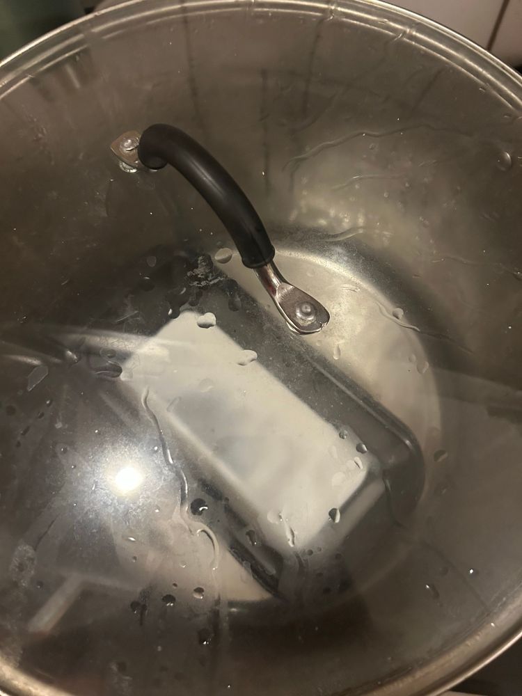 Small loaf pan with the rice noodle cooking inside of a huge water bath pot, visible through the steamy glass lid.