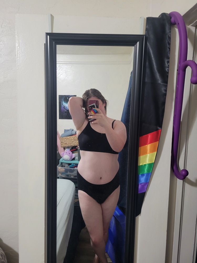 Cait in a black bra and black high-waisted panties with a cute cross-legged standing pose