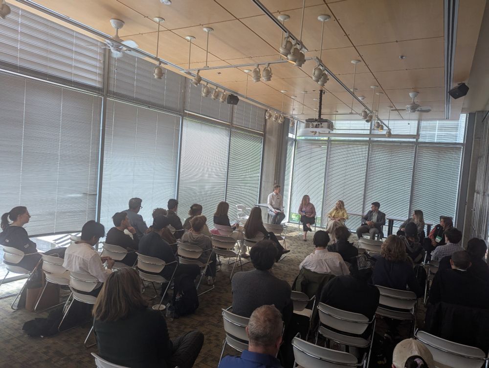 A panel of six people gives a presentation to an audience